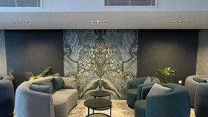 Un espace de détente moderne avec un sol en marbre, des canapés gris et turquoise, et une table ronde placée au centre.