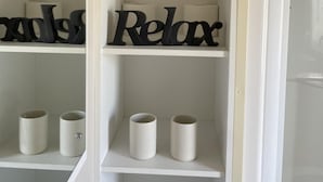A white shelving unit with two potted plants, two decorative signs spelling "Relax," and two white cylindrical containers. - Remarkable 2-bed Holiday Home in Whitstable (Whitstable)