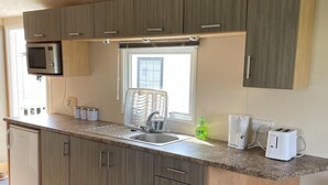 A modern kitchen with wooden cabinets, a built-in microwave, a sink, and a window above the counter. - Remarkable 2-bed Holiday Home in Whitstable (Whitstable)