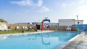 A swimming pool with a diving board, lounge chairs, and a fenced area with a building in the background. - Remarkable 2-bed Holiday Home in Whitstable (Whitstable)