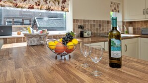 Un comptoir de cuisine avec un panier de fruits, deux verres à vin et une bouteille de vin.