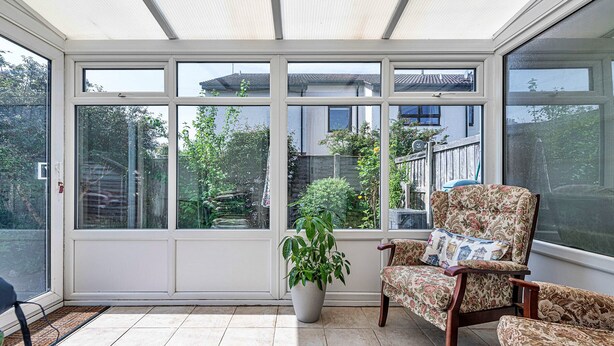 Une véranda avec de grandes fenêtres, une plante en pot et deux fauteuils à motifs.