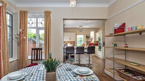 Un coin repas avec une table dressée pour quatre personnes, une cuisine en arrière-plan et une bibliothèque remplie de divers objets.