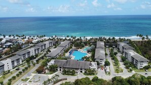 Eine Luftaufnahme eines Resorts mit mehreren Gebäuden, einem Schwimmbad und einem Strand mit Palmen.