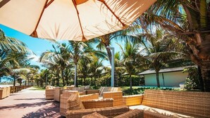 Ein Strandloungebereich mit Korbmöbeln, Palmen und einem Pool im Hintergrund.