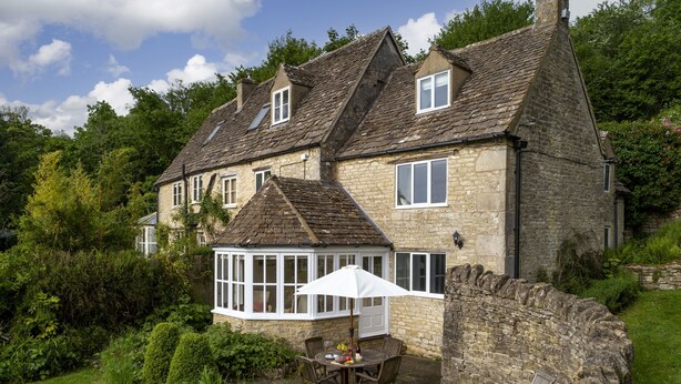 A stone house with a conservatory and a patio with a table and chairs.