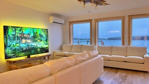 Uma sala de estar moderna com uma grande televisão de tela plana, sofás de couro branco e piso de madeira.