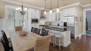 Une cuisine moderne avec des meubles blancs, un îlot central, des appareils en acier inoxydable et un coin repas avec des chaises en osier.