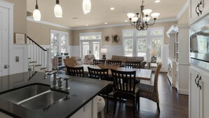 Une cuisine spacieuse avec un îlot central, un coin repas avec une grande table et des chaises, et un salon avec un canapé et des fauteuils.
