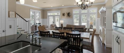 A spacious kitchen with a central island, a dining area with a large table and chairs, and a living room with a sofa and chairs.