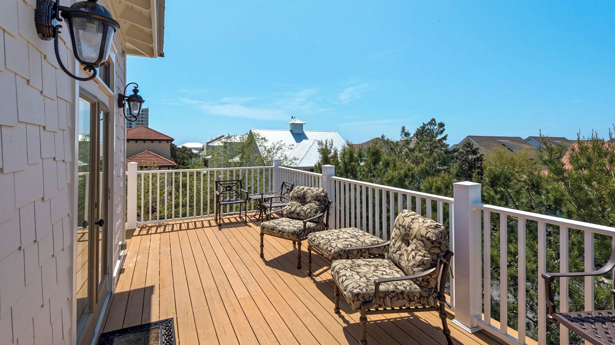 A wooden deck with outdoor furniture, a white railing, and a view of surrounding houses and trees.