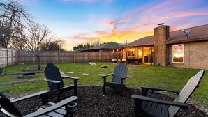 Un jardin avec deux fauteuils Adirondack, un foyer et un espace patio comprenant une table et des chaises.