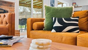 Un salon avec un canapé en cuir, un coussin à motifs verts et noirs, et une table basse en bois sur laquelle sont posés des magazines.