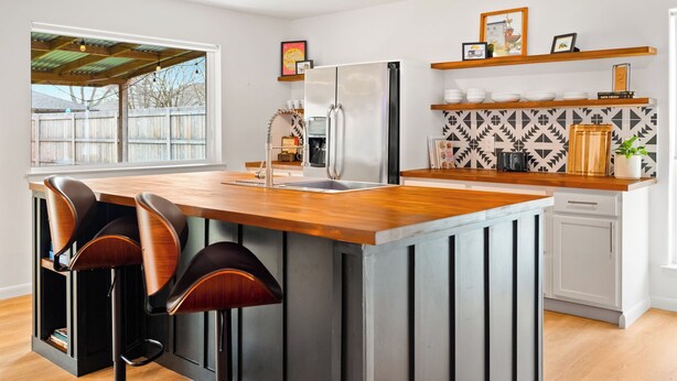Une cuisine moderne dotée d’un îlot central, de tabourets de bar, d’un réfrigérateur, d’un lave-vaisselle et d’un crédence décorée.