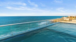 Helderblauwe lucht en een zwembad met glazen balustrade met uitzicht op de zee.