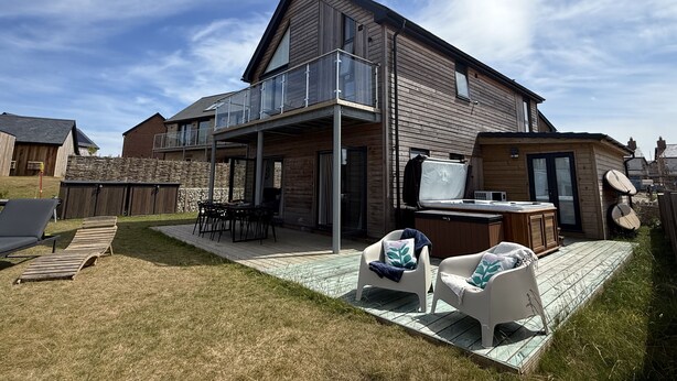 Ein modernes Haus mit Terrasse, Gartenmöbeln und einem Whirlpool.