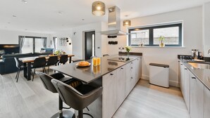 Eine moderne Küche mit einer zentralen Kochinsel, einem Essbereich mit Sofa und Stühlen sowie einem großen Fenster für natürliches Licht.
