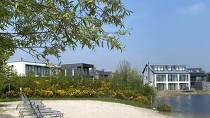 Ein Strand mit Holzliegen und modernen Gebäuden im Hintergrund.