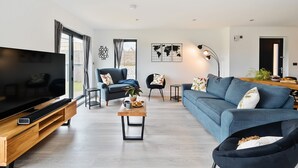 Ein modernes Wohnzimmer mit großem Flachbildfernseher, einem blauen Sofa, einem Holztisch und einem schwarzen Sessel.