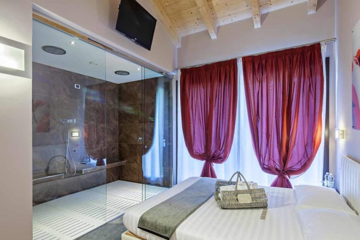 Ein modernes Hotelzimmer mit einem großen Bett, einer Duschkabine aus Glas und einem an der Decke befestigten Fernseher.