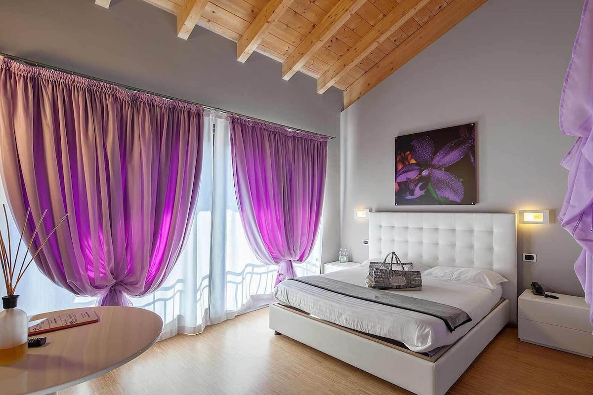 Ein Schlafzimmer mit einem großen Bett, einem Nachttisch und einem Fenster mit violetten Vorhängen.