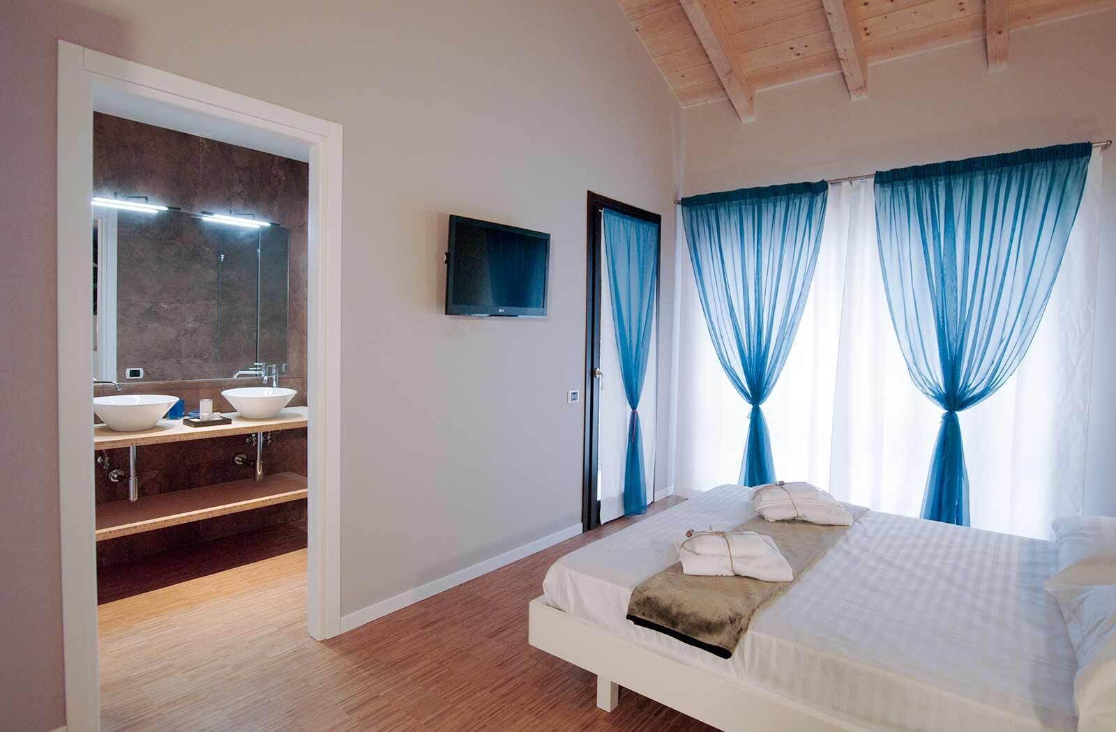 Un dormitorio con cama, televisor, baño con espejo y cortinas azules.
