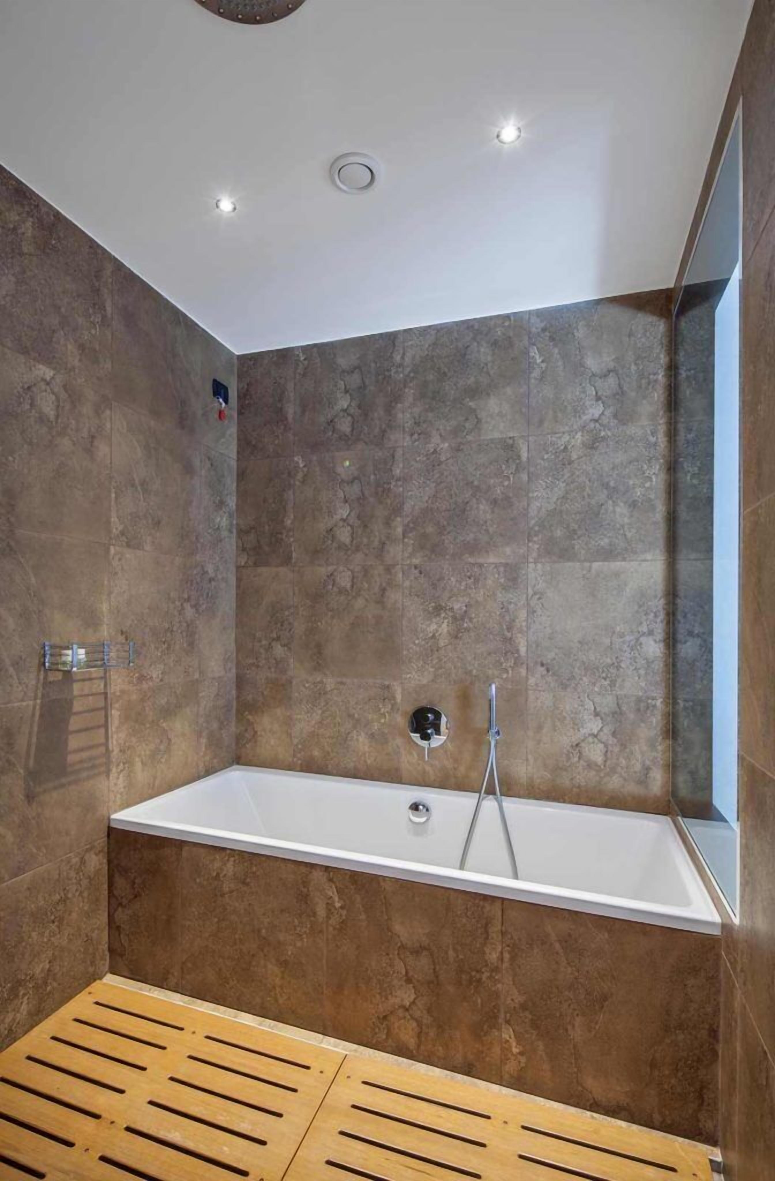 Un baño moderno con una bañera independiente, paredes de piedra y suelo de madera.