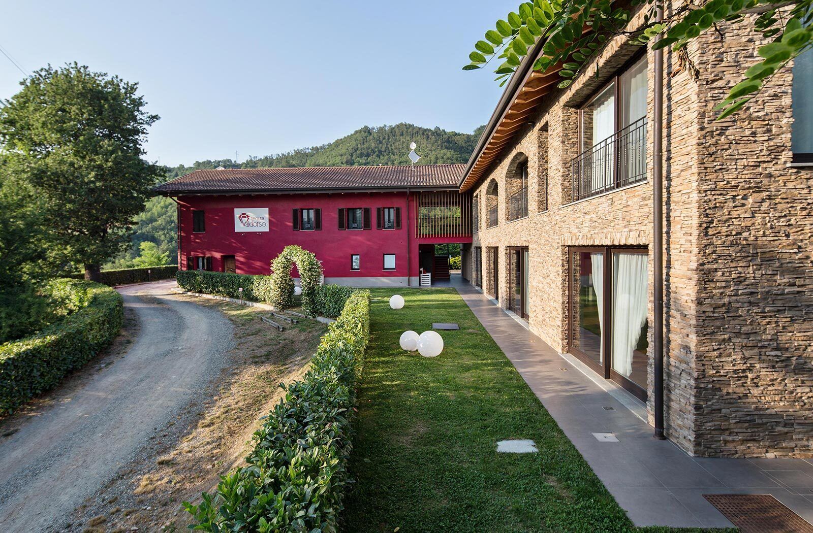 A red building with a stone facade, a gravel driveway, and a well-maintained lawn with white spherical decorations.