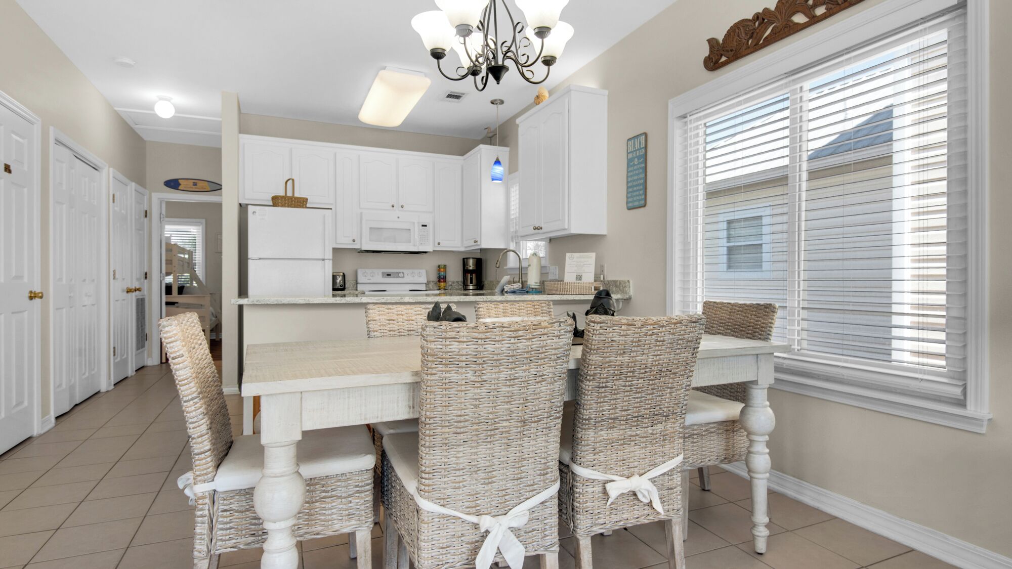 A kitchen with white cabinets, a central island, wicker chairs, and a chandelier.
