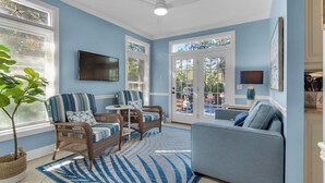 A living room with wicker furniture, a blue sofa, and a large window overlooking a backyard.