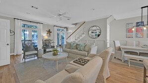 A spacious living room with a high ceiling, a staircase, and a dining area.