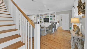 A modern interior with a wooden staircase, a dining area with chairs, and a TV on a white cabinet.