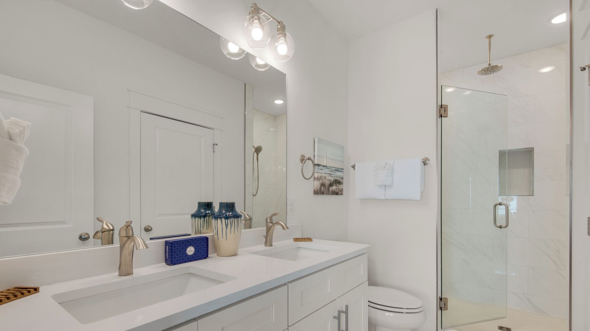 A modern bathroom with a double sink, a toilet, and a glass-enclosed shower area.