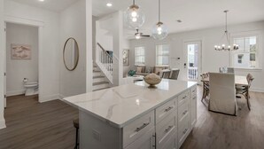 A modern kitchen with a marble island, pendant lights, and a dining area with a wooden table and chairs. - Spacious 4BR With 2 Master Suites, Golf Cart, .3 Miles to Beach - Sleeps 15 (Santa Rosa Beach)