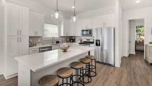 A modern kitchen with white cabinetry, a central island with stools, stainless steel appliances, and pendant lighting. - Spacious 4BR With 2 Master Suites, Golf Cart, .3 Miles to Beach - Sleeps 15 (Santa Rosa Beach)