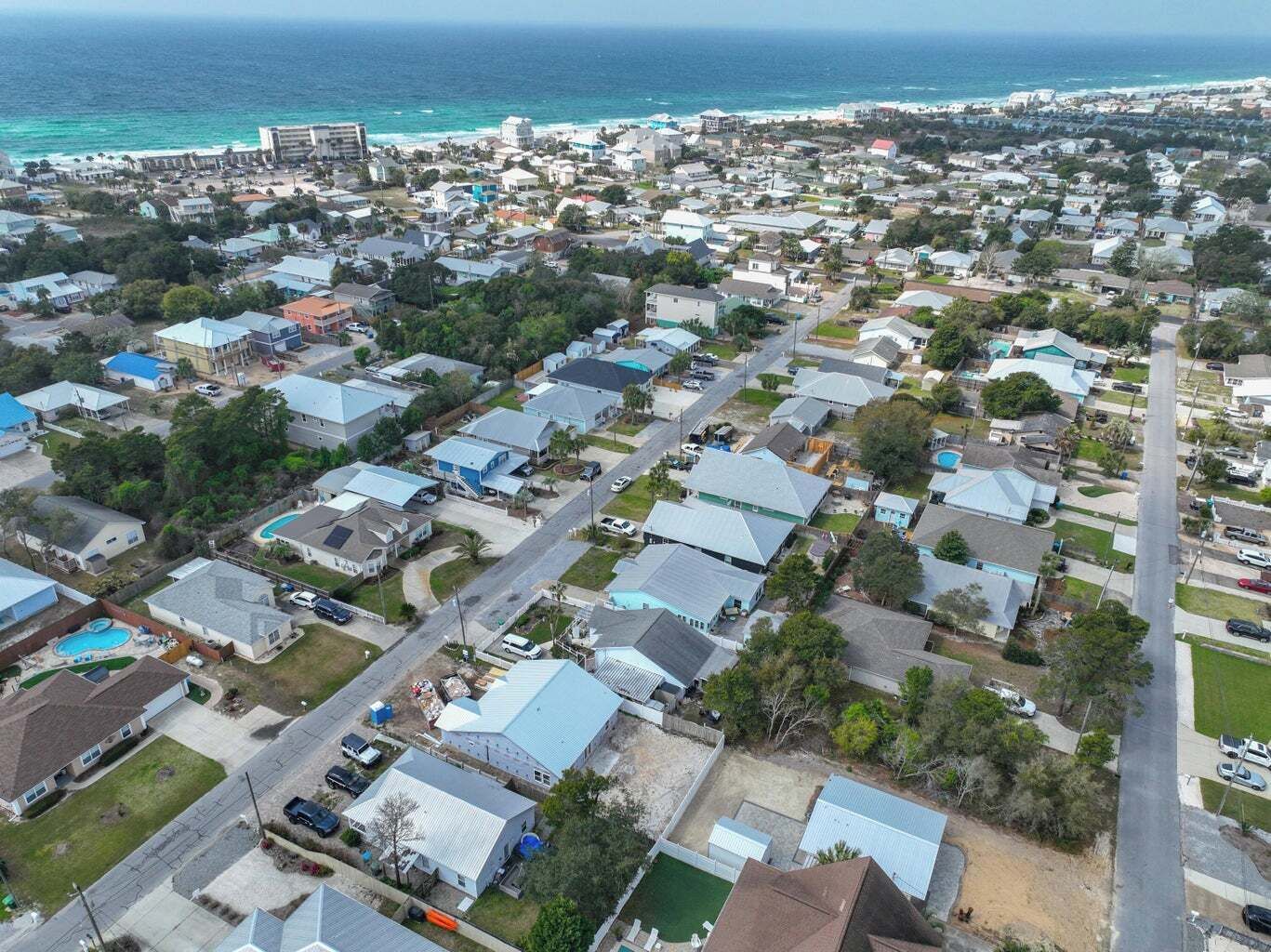 Vista aérea de una zona residencial costera con casas, carreteras y una playa al fondo.