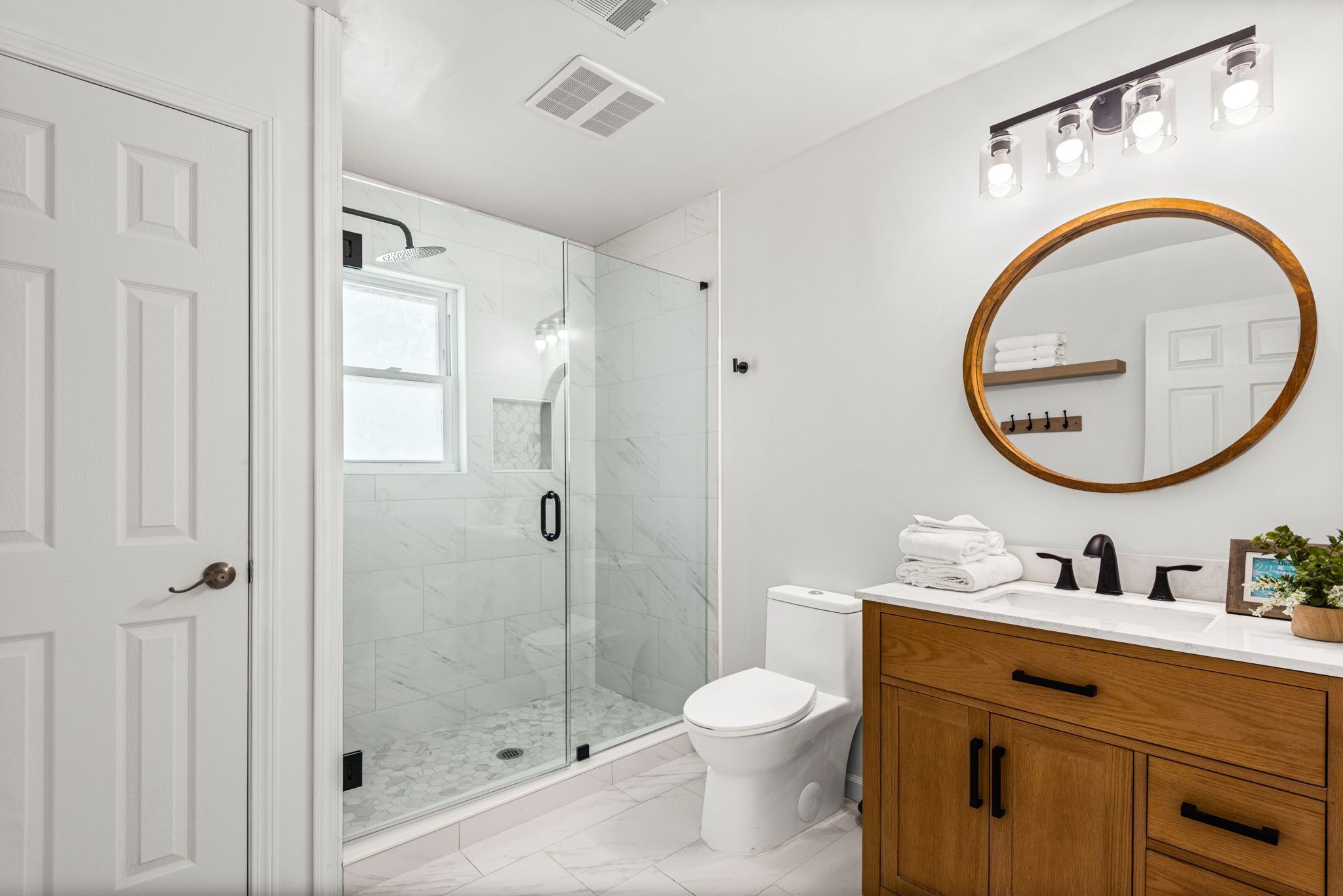 A modern bathroom with a glass shower enclosure, a white toilet, a wooden vanity with a mirror, and a white sink.