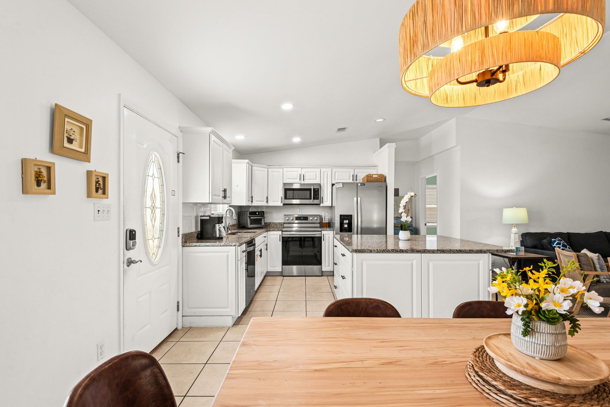 Une cuisine moderne avec des meubles blancs, des appareils en acier inoxydable et un coin repas comprenant une table et des chaises en bois.