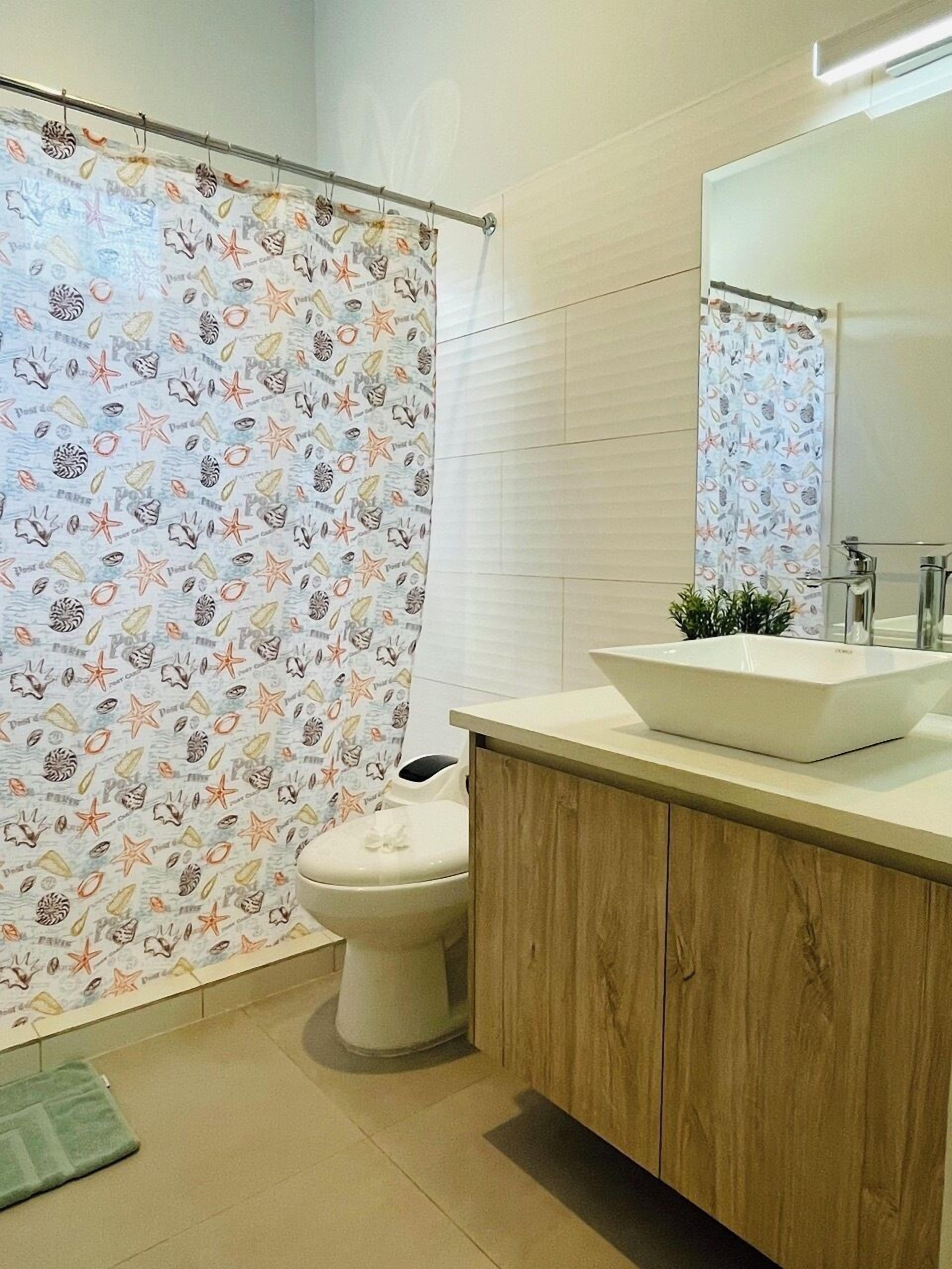 A bathroom with a shower curtain featuring a sea-themed pattern, a white toilet, a wooden vanity with a sink, and a mirror above the sink.