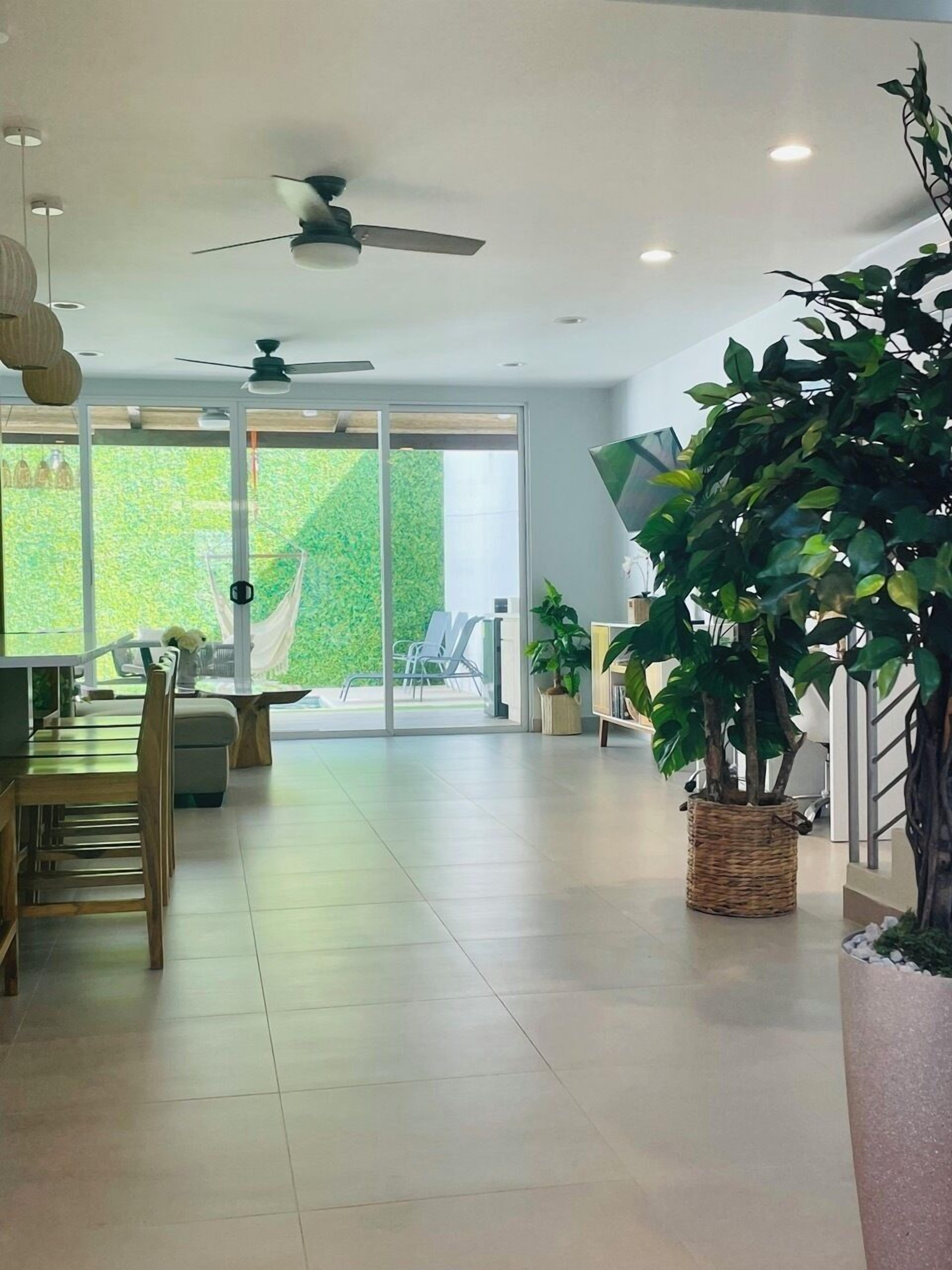 A spacious living area with a dining table, chairs, a large potted plant, and a sliding glass door leading to an outdoor area.