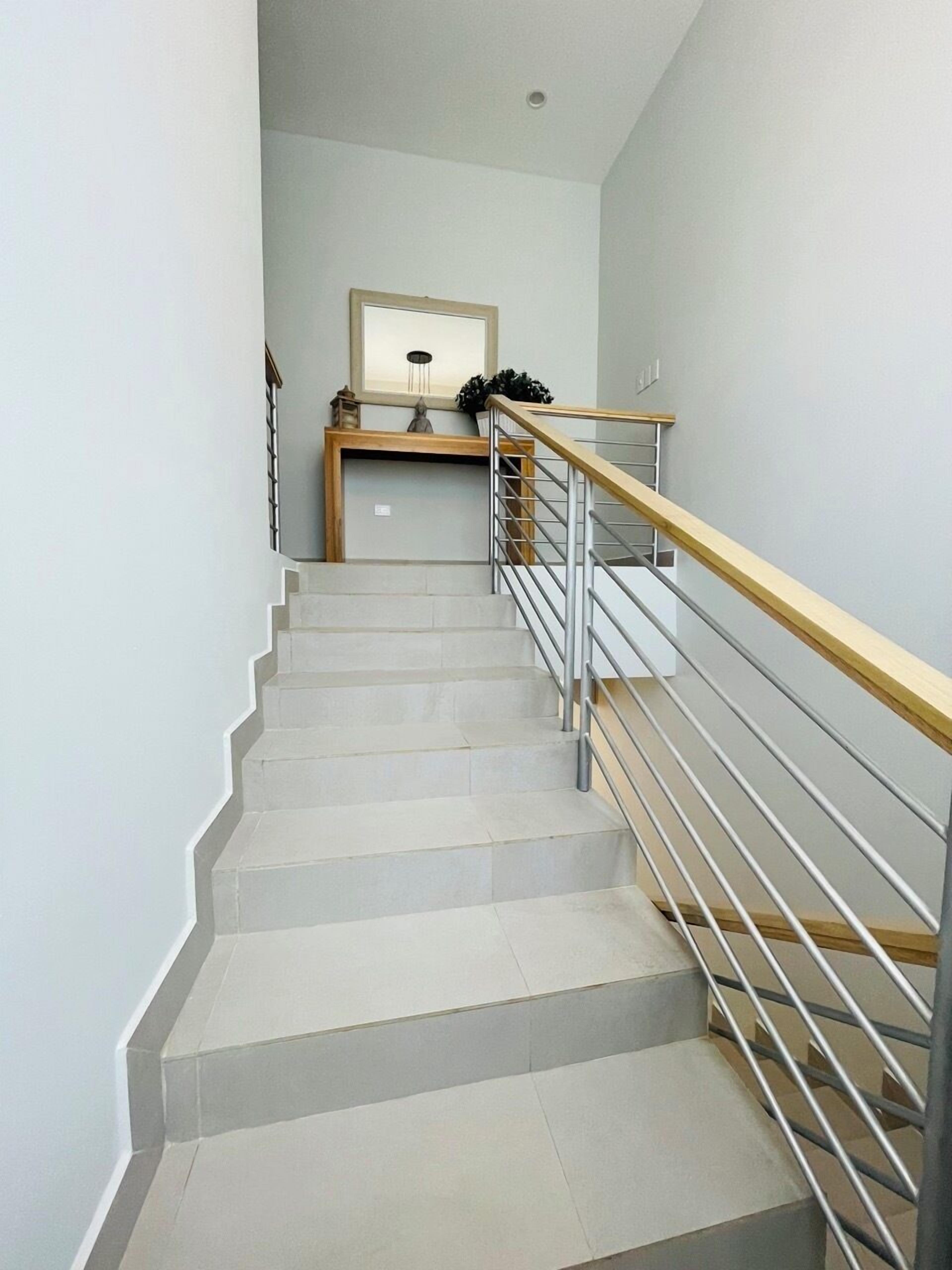 A staircase with a wooden handrail and metal balusters, leading to a landing with a framed mirror and a small table with decorative items.
