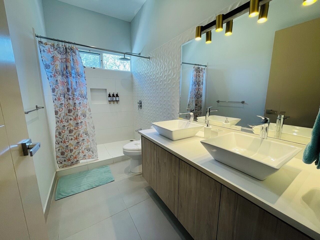 A modern bathroom with two sinks, a shower, and a toilet.