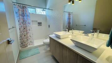 A modern bathroom with two sinks, a shower, and a toilet.
