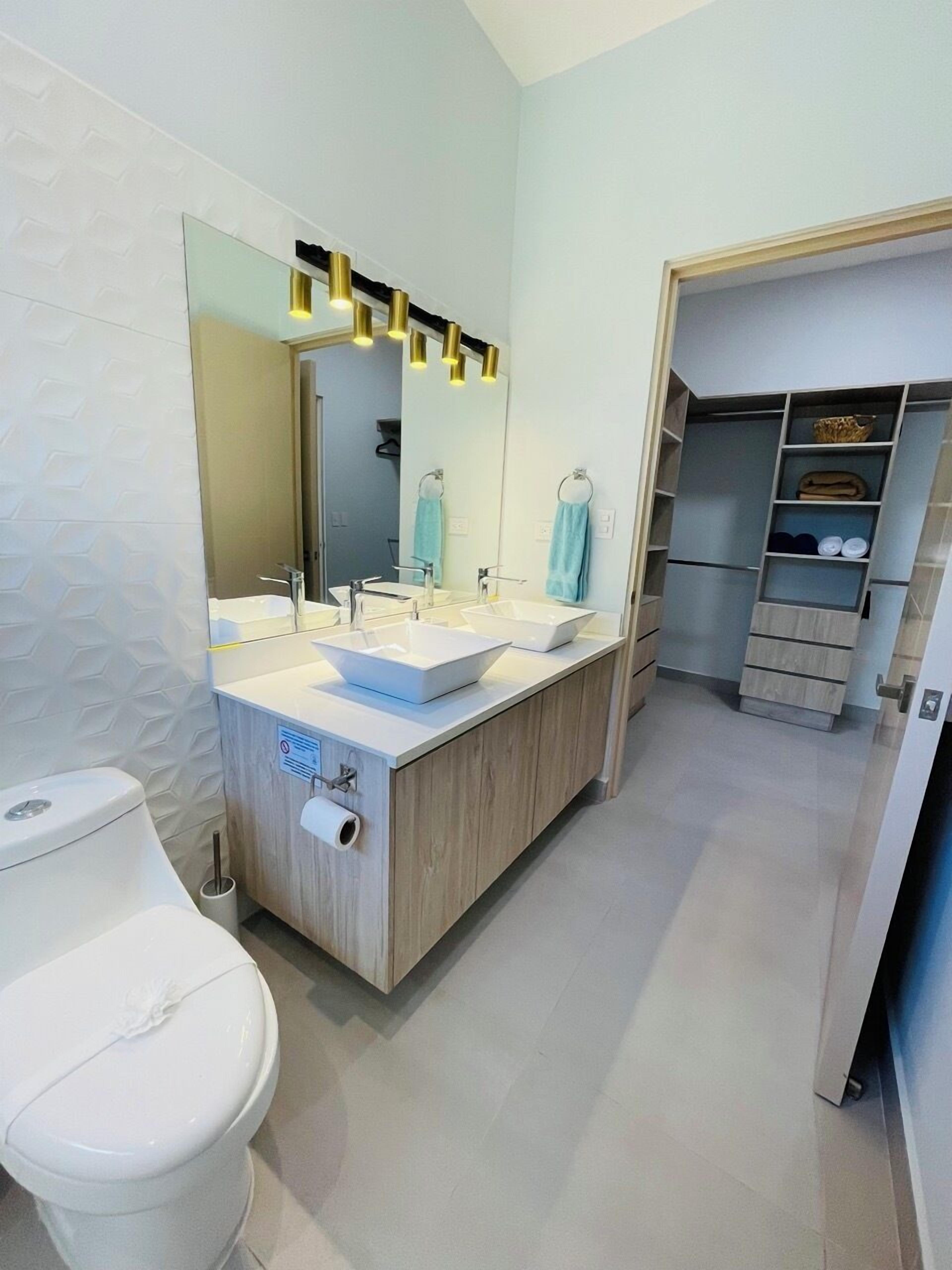 Une salle de bain moderne avec des toilettes blanches, un lavabo avec un miroir et un meuble-lavabo en bois.