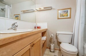 A bathroom with a wooden vanity, a sink, a toilet, a shower curtain, and a framed picture on the wall.