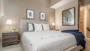 A neatly arranged bedroom with a large bed, two bedside tables with lamps, a mirror, and framed artwork on the wall. - 3 Bedroom Centrally Located Ski In/Ski Out Condo in Panorama (Panorama)