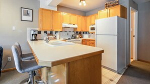 A compact kitchen with wooden cabinets, a white refrigerator, and a bar stool. - 3 Bedroom Centrally Located Ski In/Ski Out Condo in Panorama (Panorama)
