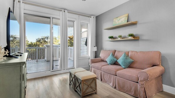A living room with a striped sofa, a small table, and a bench. There is a sliding glass door leading to an outdoor balcony. - Steps From Baytowne Wharf With Pool & Private Beach Access (Miramar Beach)
