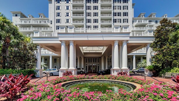 A large hotel with a central entrance, multiple balconies, and a fountain surrounded by pink flowers. - Steps From Baytowne Wharf With Pool & Private Beach Access (Miramar Beach)