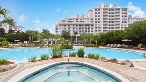 A swimming pool with lounge chairs and a hot tub, surrounded by palm trees and a large hotel building in the background. - Steps From Baytowne Wharf With Pool & Private Beach Access (Miramar Beach)